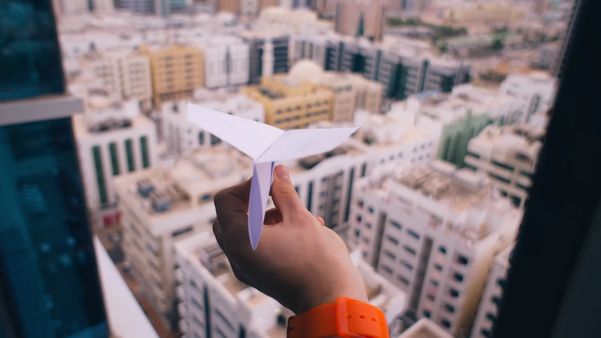 Hand launching a white paper airplane above a city of rooftops