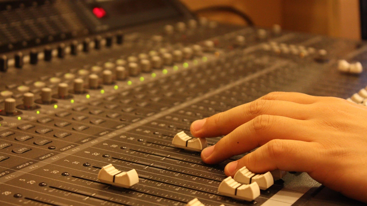 Hand moving the sliders of a studio mixing console