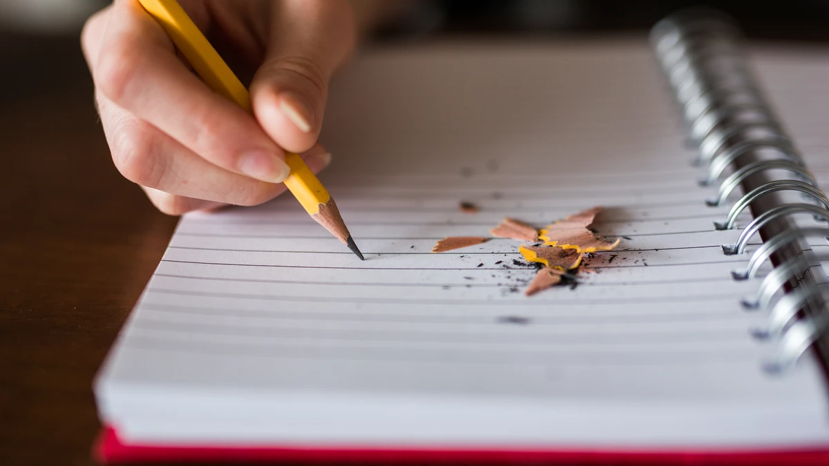 Hand writing with a pencil in a spiral notebook, with pencil shavings on the page