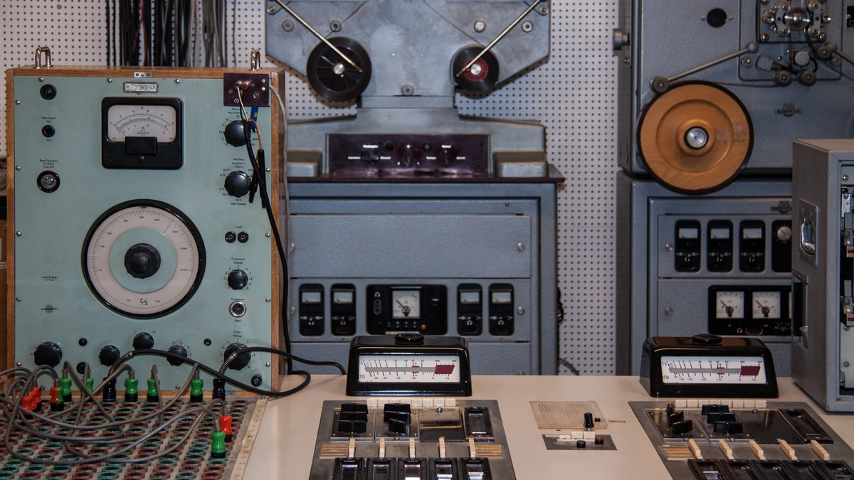 Vintage studio recording desk with reel-to-reel tape machines, level meters and a bank of faders