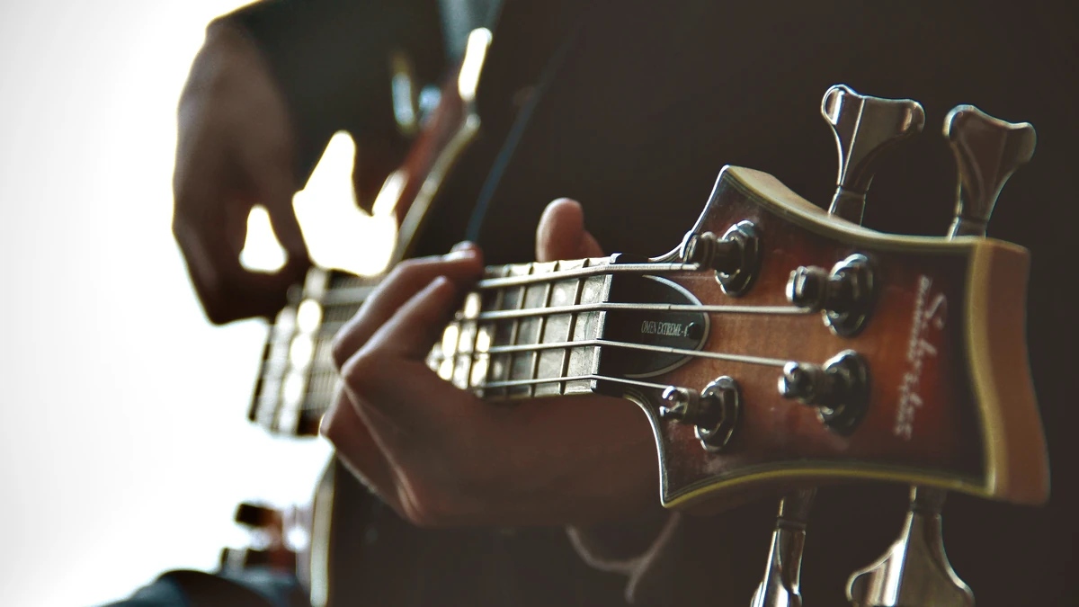 Hands on the neck and tuners of an electric bass guitar in warm light