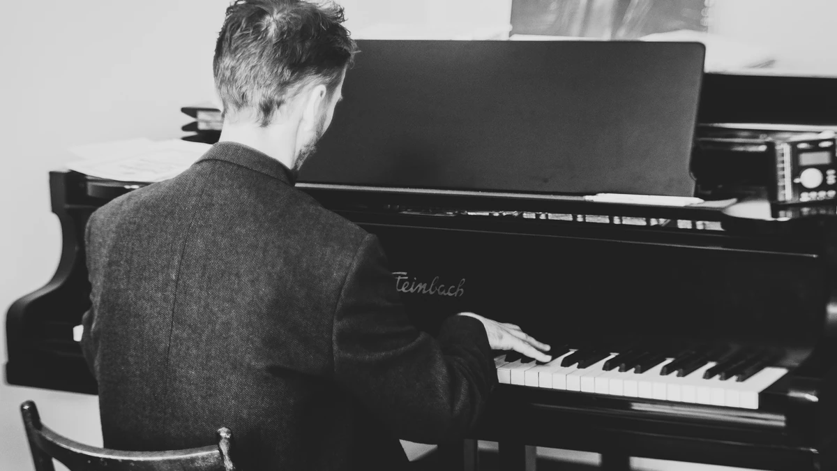 Pianist seen from behind playing an upright piano, in black and white